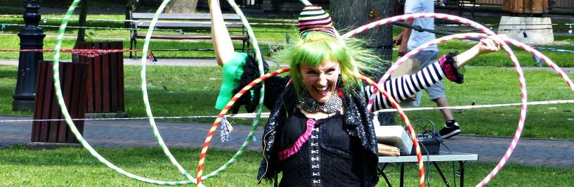kolorowo ubrana aktorka tańcząca z hula-hoopami na trawniku w parku miejskim